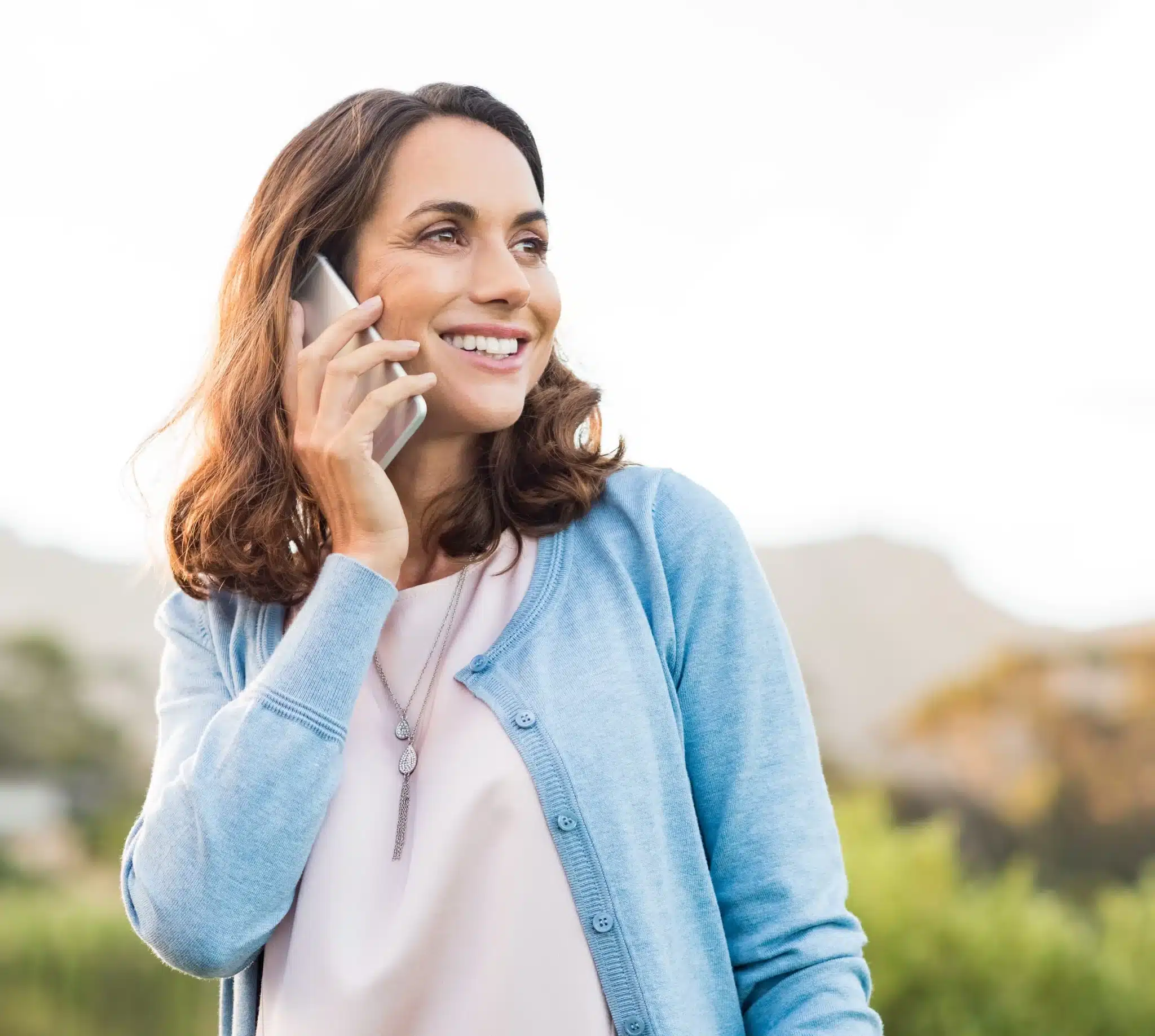 Smiling person holding a phone to their ear outdoors.