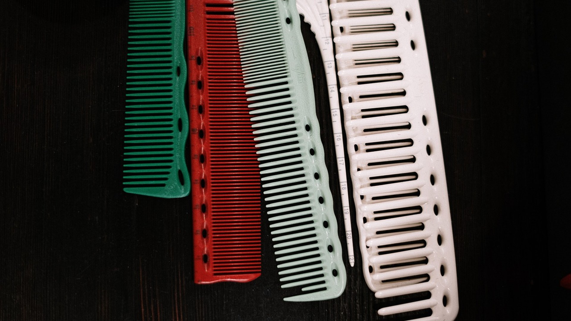 Close-up of fine-tooth combs lined up on a dark surface, illustrating the tooth-gap variation that determines whether a nit comb can extract lice eggs.