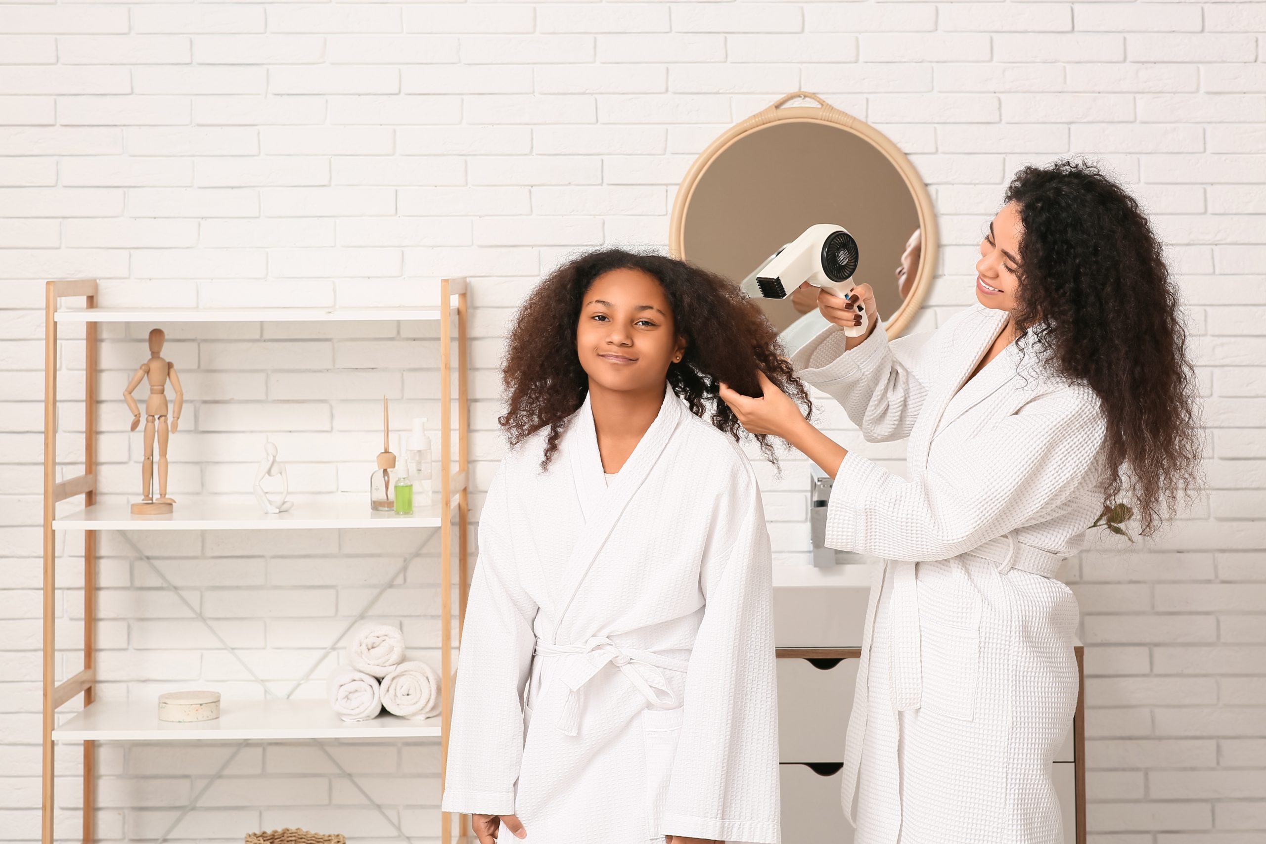 Mother blow drying her daughter's hair in a bathroom