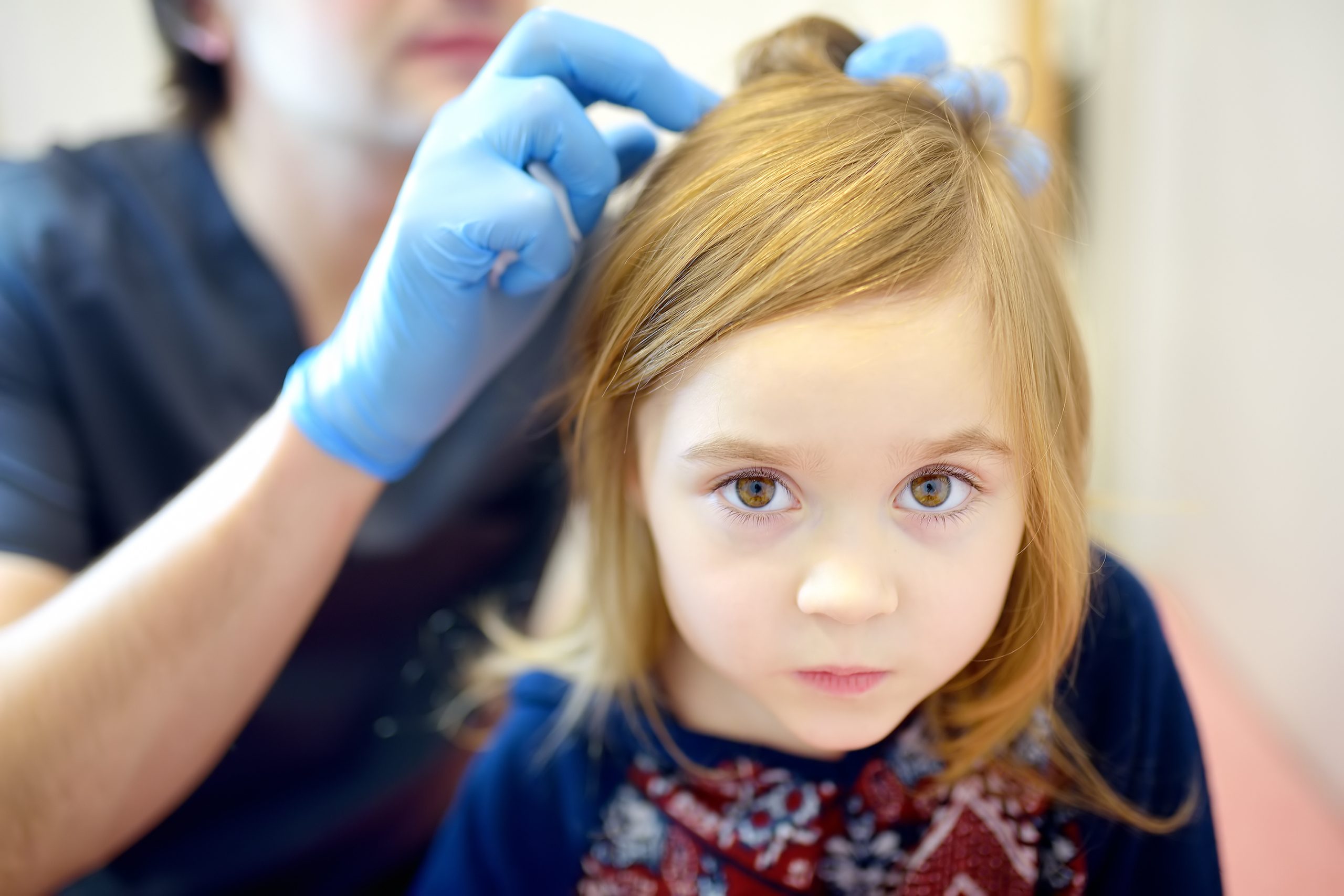 Doctor at a Broward County lice clinic combing through a young child's hair to inspect for lice and nits