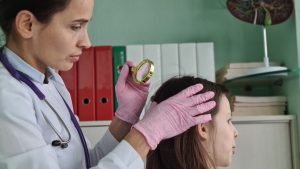 Pediatrician using a magnifying glass to inspect a Broward County child's scalp under clinical light, the moment most families realize a head lice case has outlasted home remedies and needs a trained eye on the parasite.