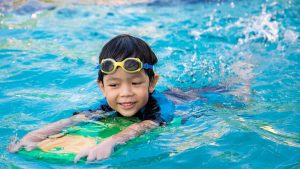 A group of young children swimming underwater together in a community pool on a sunny South Florida afternoon, hair fanned out around their heads.