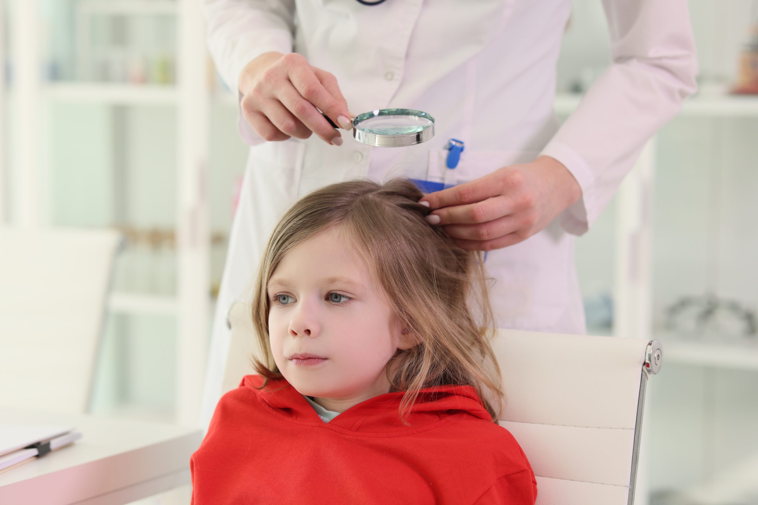 Pediatrician looks for lice on head of little girl in chair