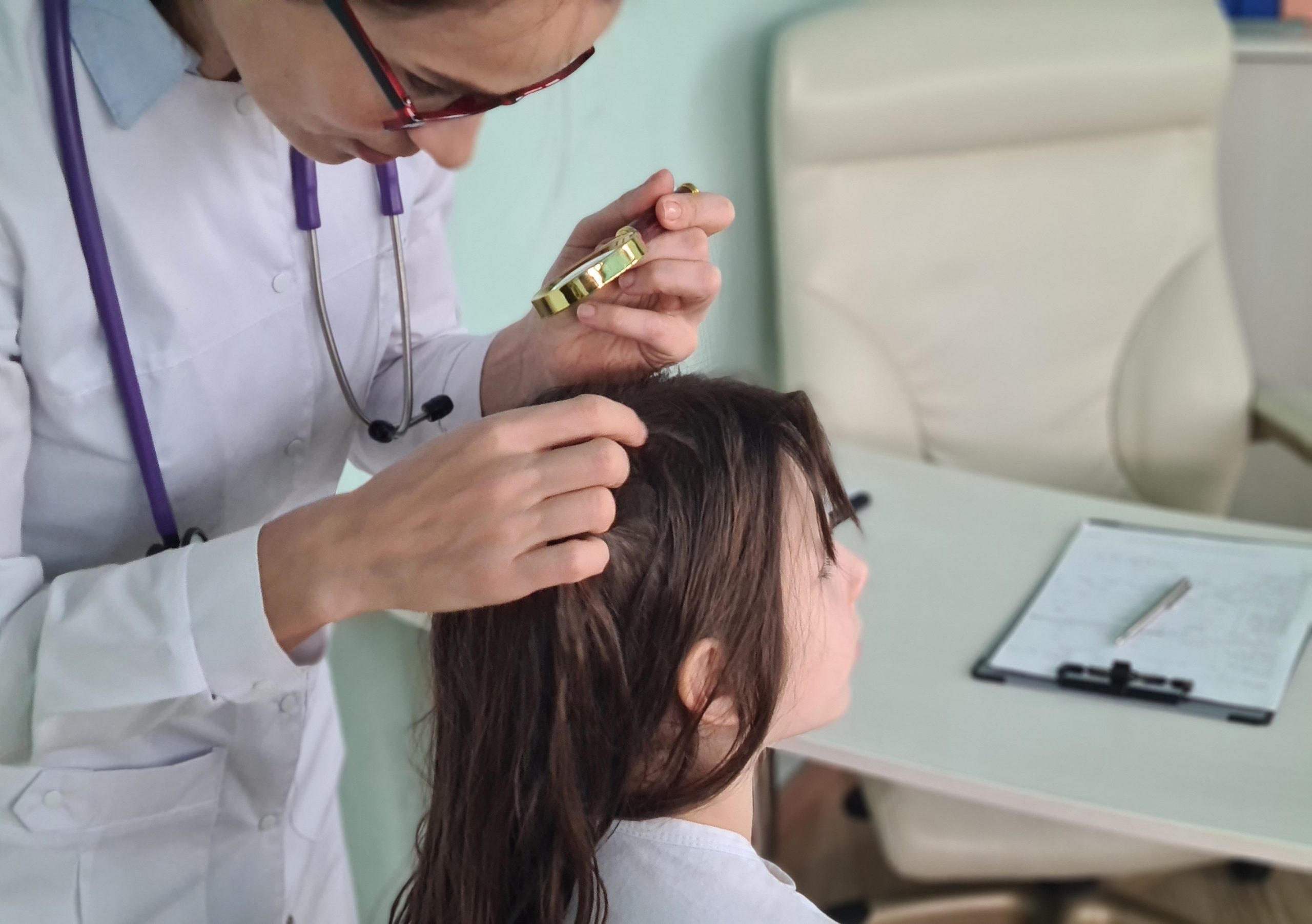 A clinician examines a young child's scalp for head lice with a magnifying glass in a bright medical clinic, the professional lice screening this article describes