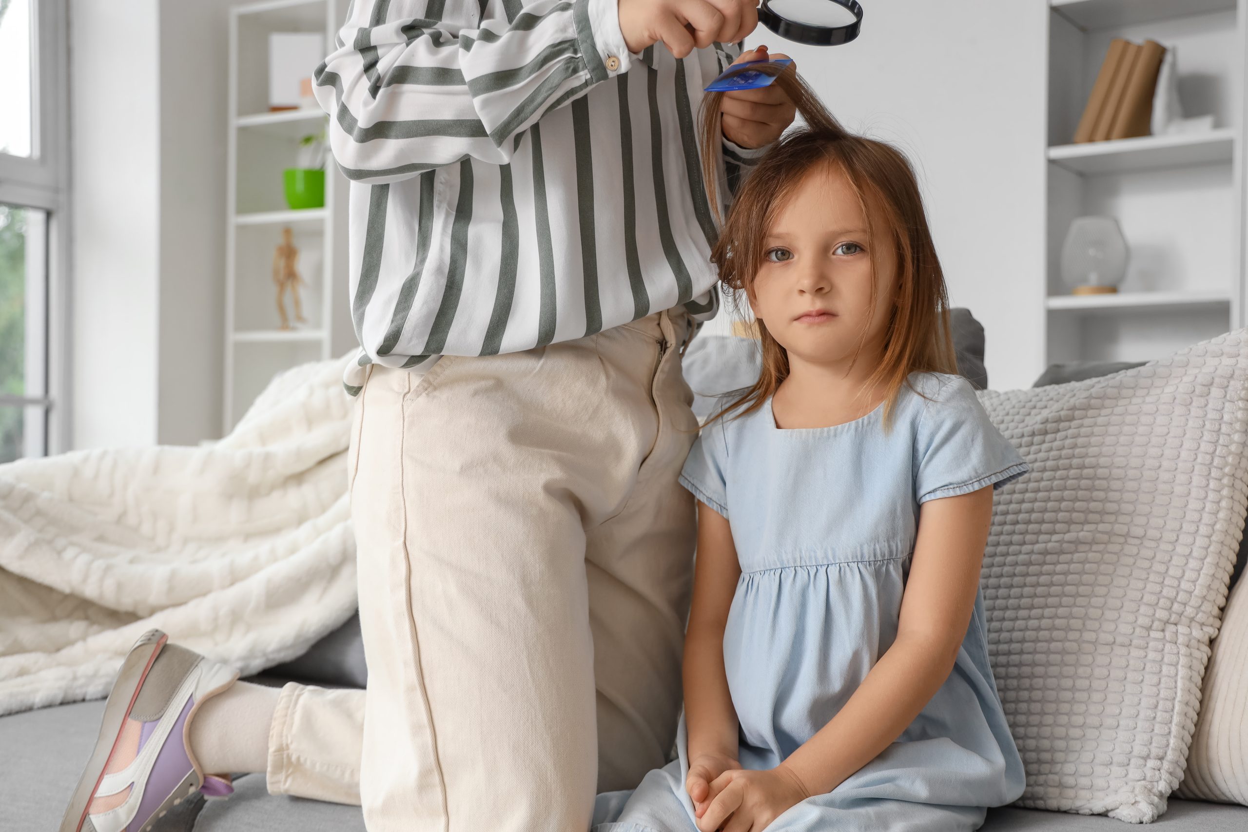 A parent combs a young child's hair with a metal nit comb at home to remove head lice and eggs, the at-home removal routine this article describes