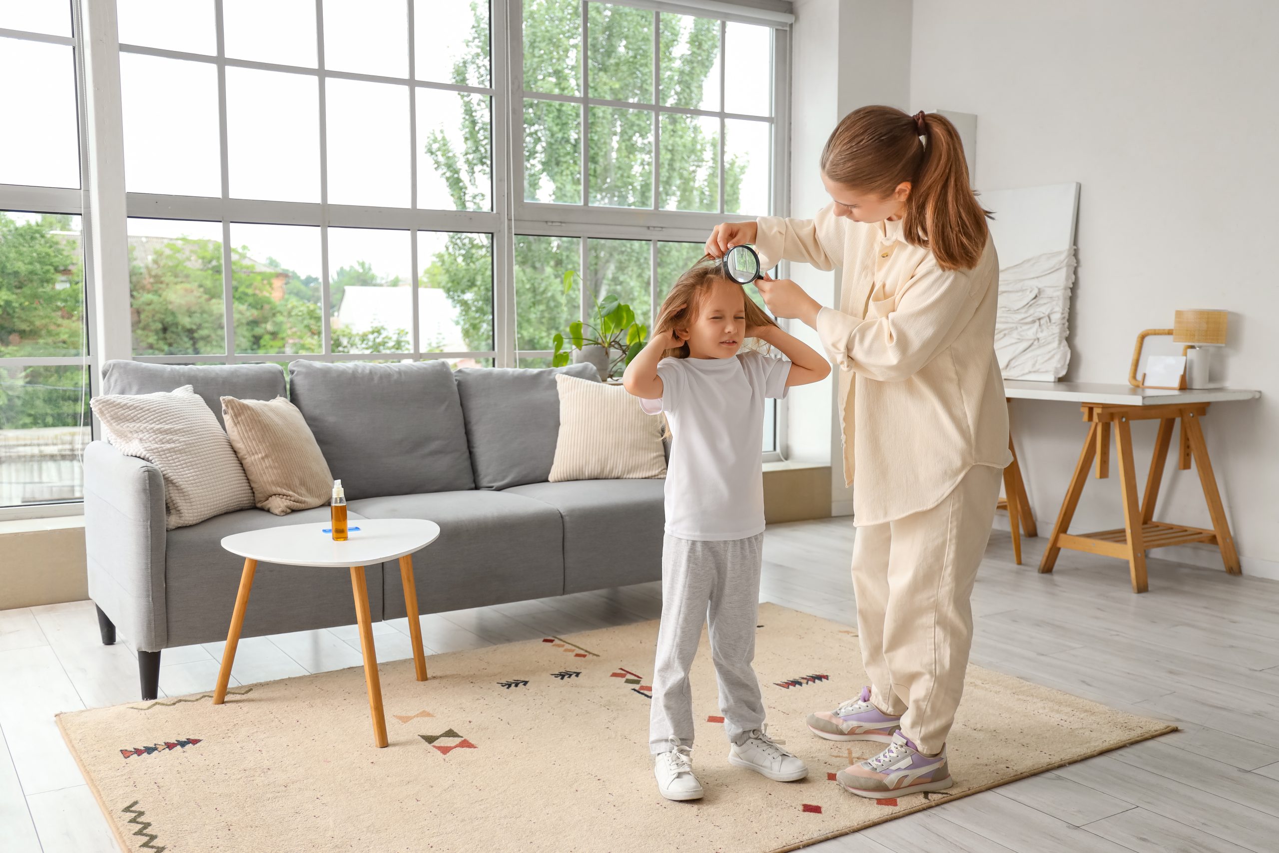 A parent calmly checks a young child's scalp with a magnifier at home to look for head lice, the reassuring at-home head check this article describes