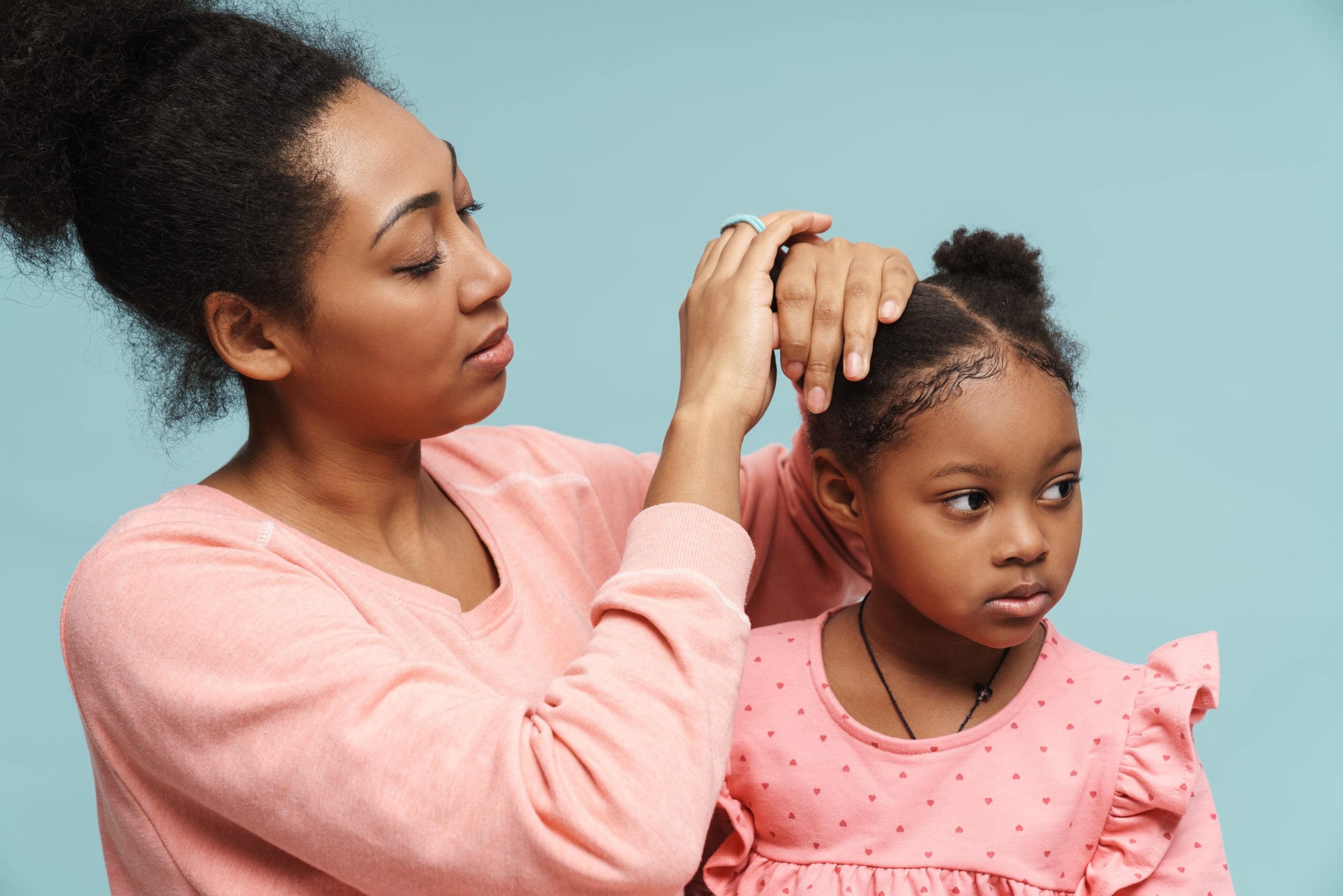 Woman Styling Girl's Hair Against Pale Blue Background