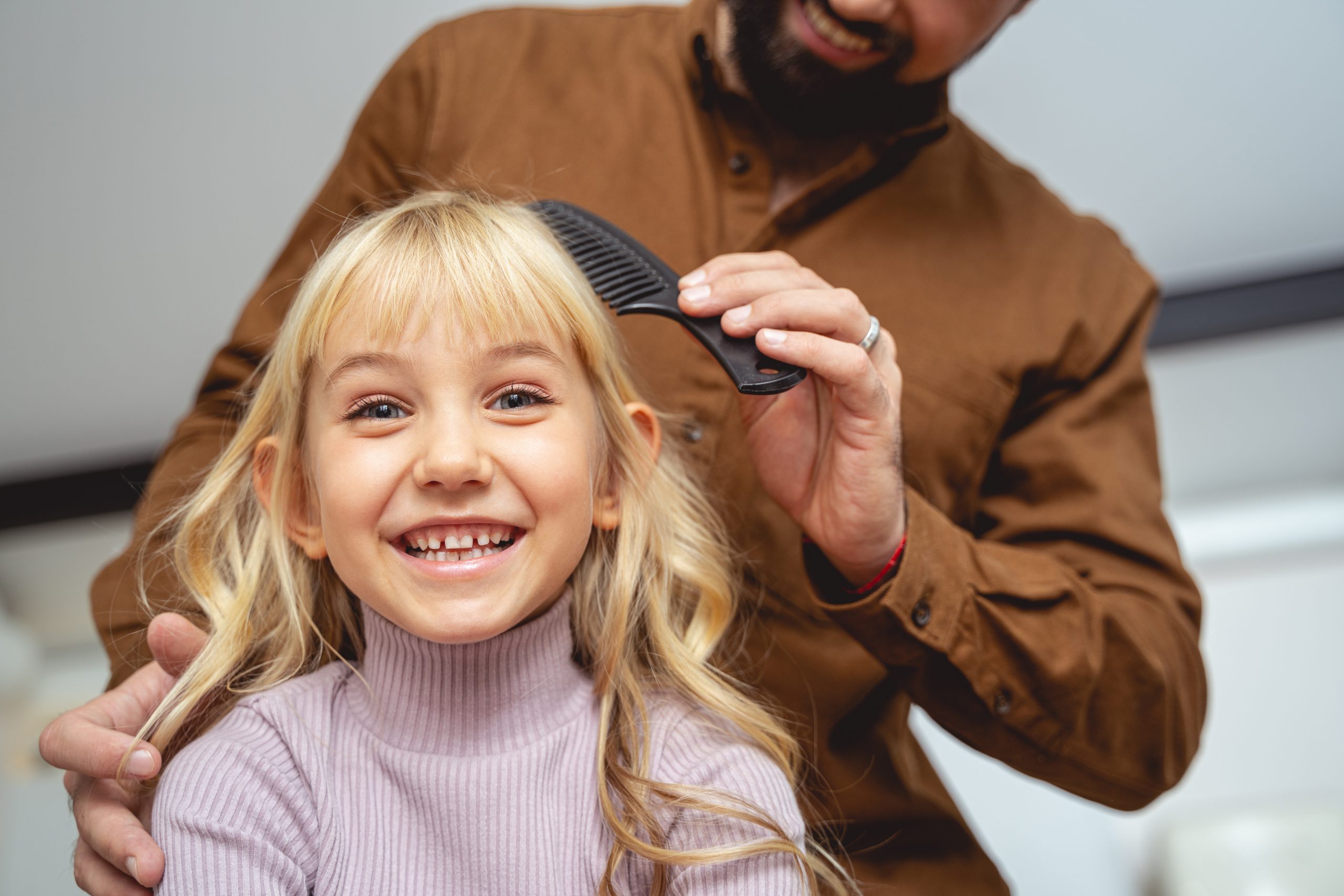 Father combing hair of his cheerful daughter