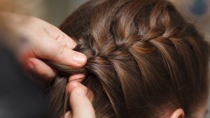Broward County mother carefully braiding her school-age daughter's hair into a tight French braid during a lice notice week.