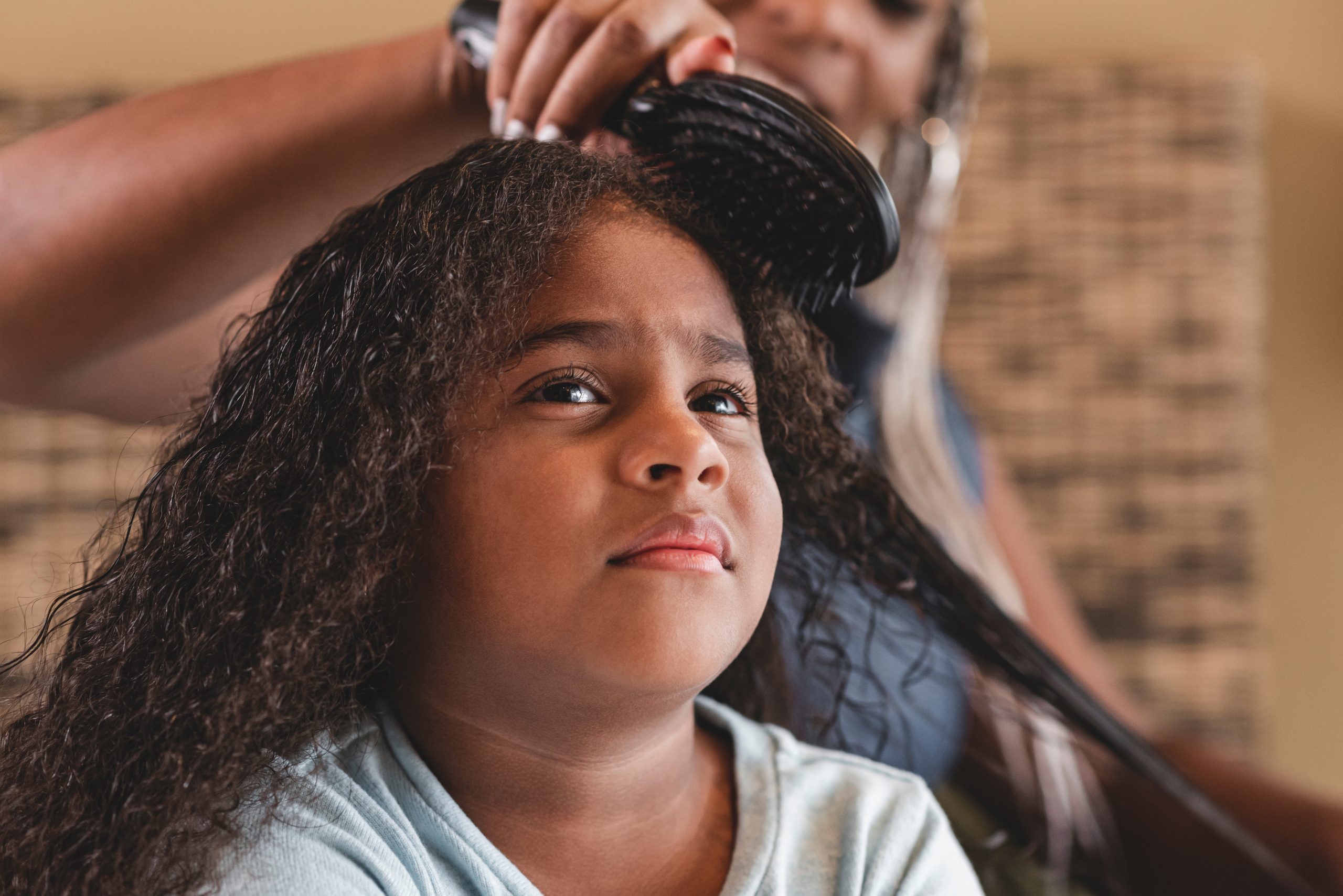 Parent brushing through a young girl's long dark textured hair at home