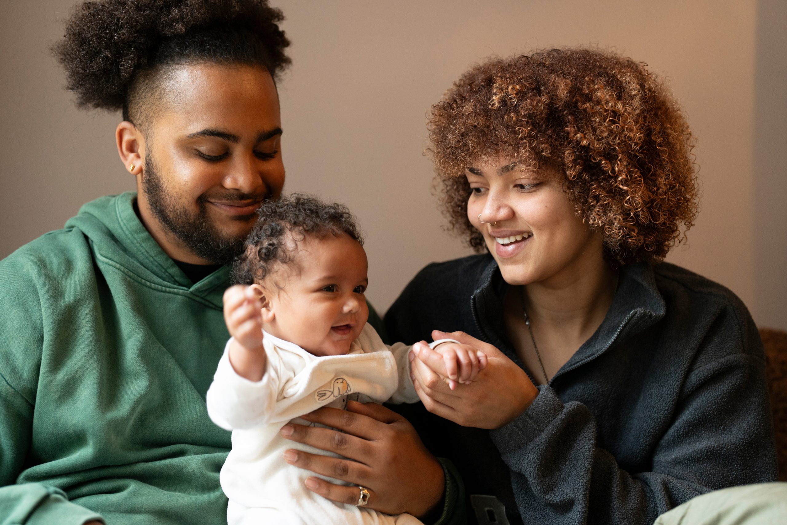Two parents sitting together at home holding their smiling infant daughter