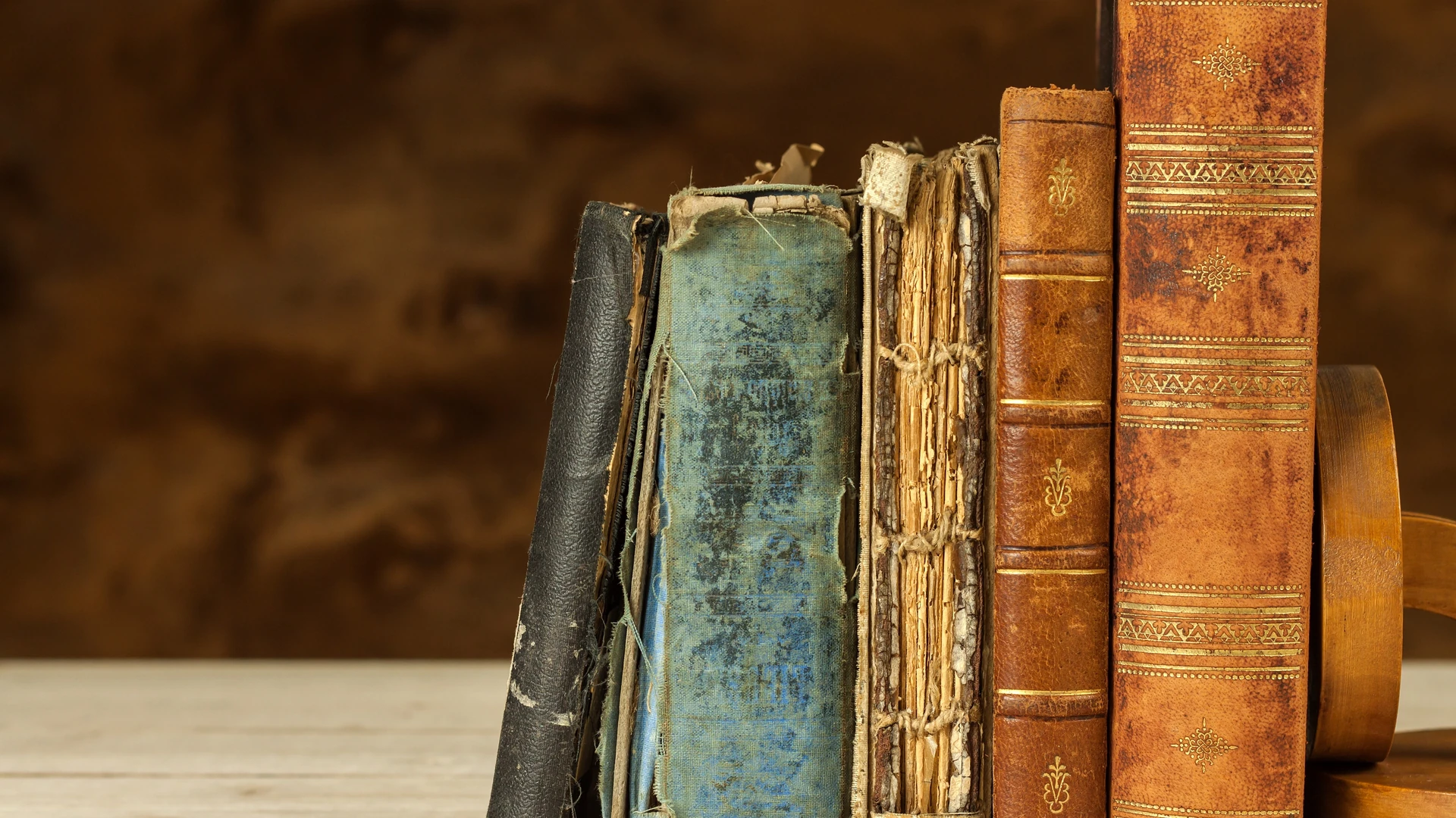 Row of worn books with frayed spines standing on a light surface