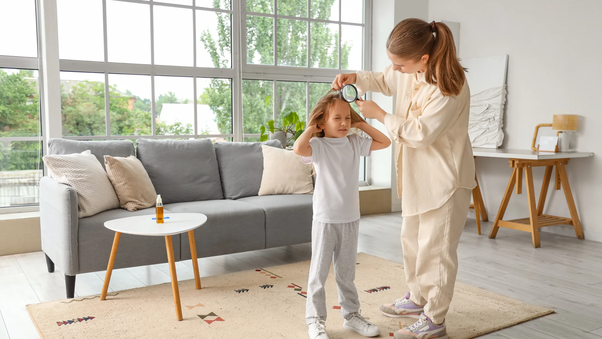 Person examining another person's hair with a magnifying glass beside a sofa